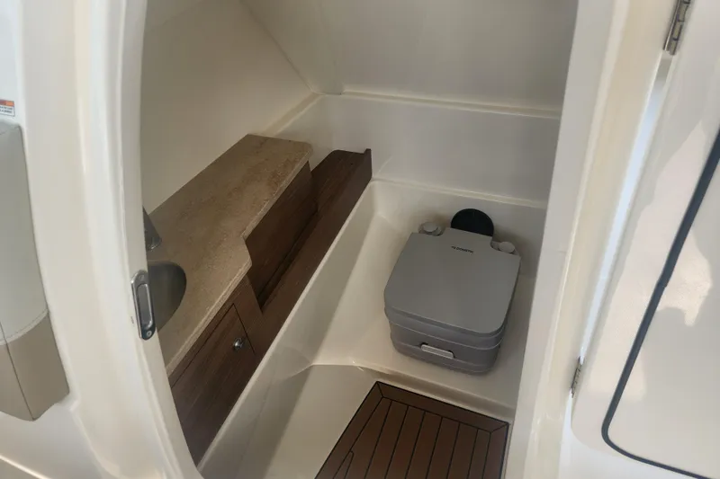Slide: The Image of 2021 Boston Whaler 280 Vantage interior with compact marine toilet and wooden cabinetry. - 11
