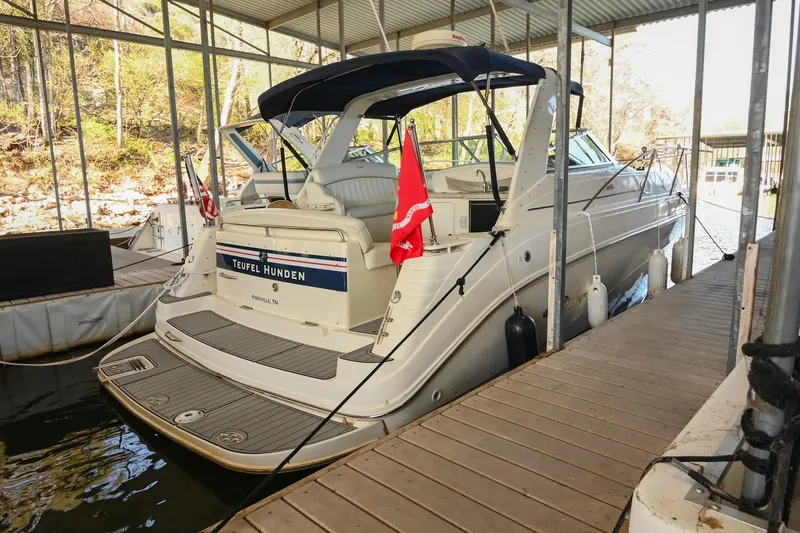 Slide: The Image of 2000 Rinker Fiesta Vee 330 boat docked under a covered marina with flags displayed. - 4
