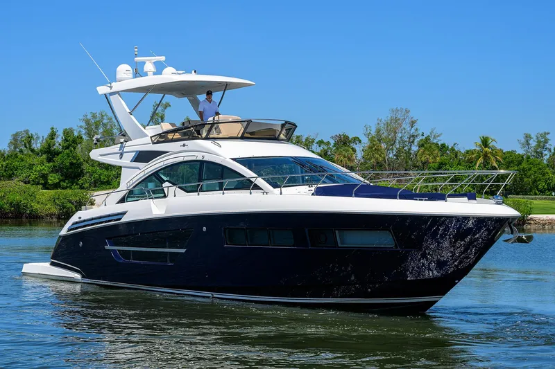 Slide: The Image of 2018 Cruisers 60 Cantius Fly yacht cruising on a sunny day, surrounded by lush greenery. - 4
