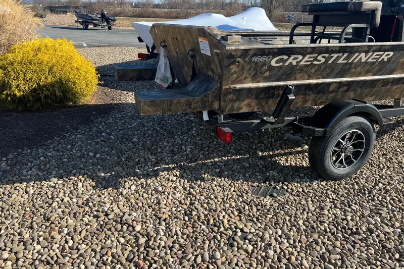 Slide: The Image of 2025 Crestliner 1660 Retriever FCC boat on trailer, parked on gravel. - 2