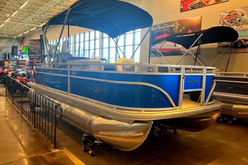 The Image of A blue pontoon boat with a sunshade is displayed in a showroom. - 0