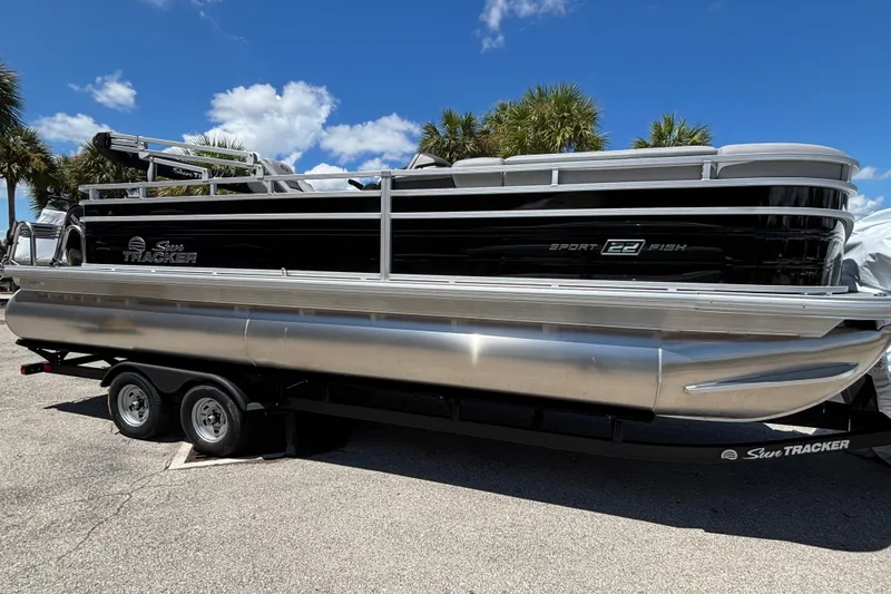 The Image of 2026 Sun Tracker SportFish 22 DLX pontoon boat on trailer, parked under blue sky. - 0