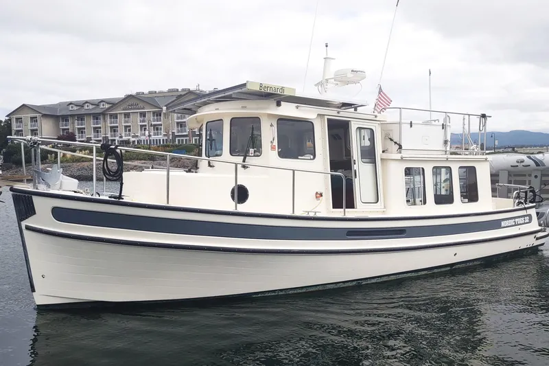 The Image of 2004 Nordic Tug 32 boat docked near a waterfront hotel. - 0