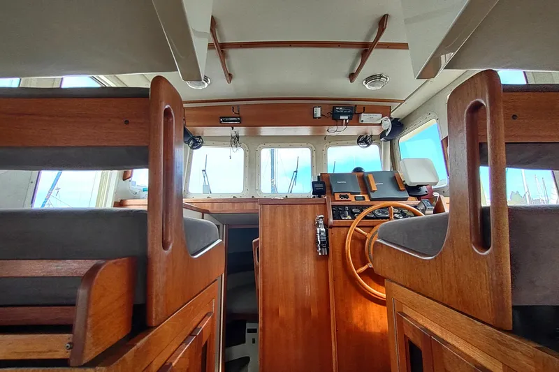 Slide: The Image of 2004 Nordic Tug 32 interior with wooden helm and seating, showcasing nautical design. - 23