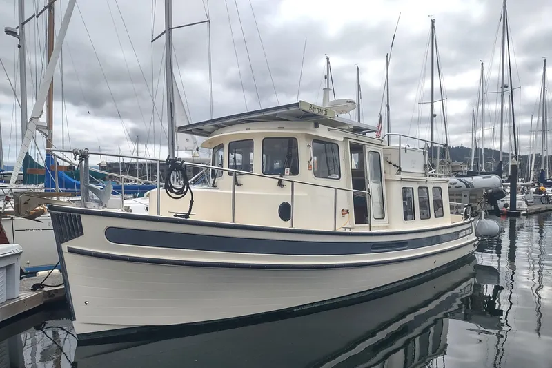 Slide: The Image of 2004 Nordic Tug 32 docked in a marina, surrounded by sailboats under cloudy skies. - 4