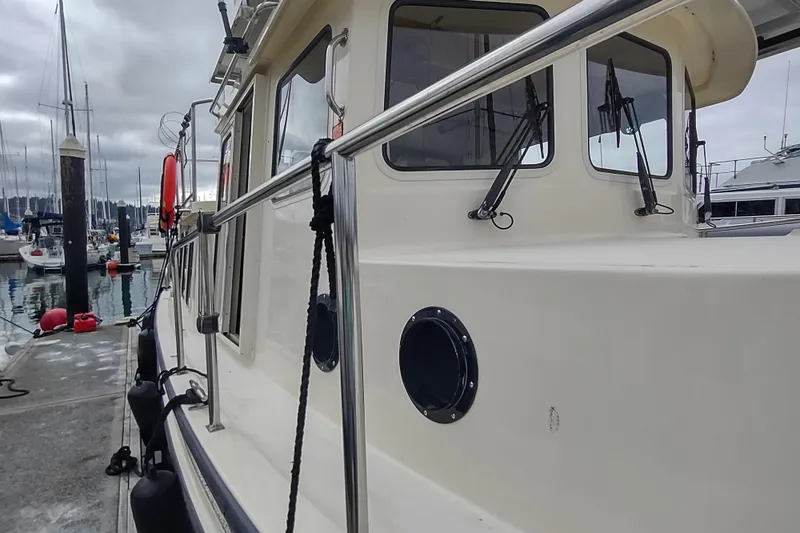 Slide: The Image of 2004 Nordic Tug 32 docked at marina, showcasing side view and cabin windows. - 8