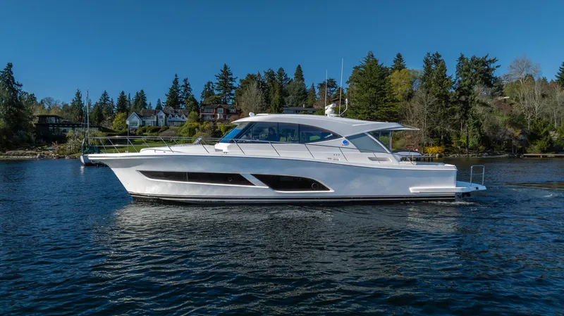 Slide: The Image of 2024 Riviera 505 SUV yacht cruising on a serene lake with forested shoreline. - 42