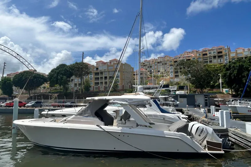 The Image of 2021 Tiara Yachts 34 LS docked at marina, clear sky, waterfront buildings. - 0
