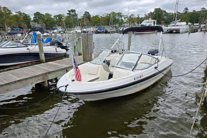 Slide: The Image of 2011 Bayliner 180 Bowrider docked at marina, American flag displayed, calm water background. - 21