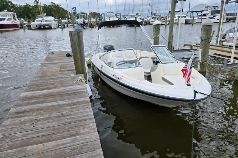 Slide: The Image of 2011 Bayliner 180 Bowrider docked at marina, featuring open bow seating and American flag. - 23