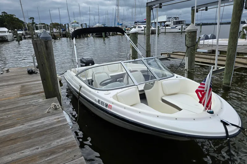 Slide: The Image of 2011 Bayliner 180 Bowrider docked at marina with American flag, overcast sky. - 3