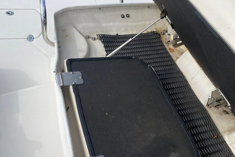 Slide: The Image of Open storage compartment on a 2007 Monterey 234FSX boat, featuring black mat and metal hinges. - 23