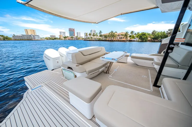 Slide: The Image of The image shows the spacious aft deck of a 2026 Cruisers Yachts 50 GLS with comfortable seating and a table, surrounded by water and a cityscape in the background. - 24