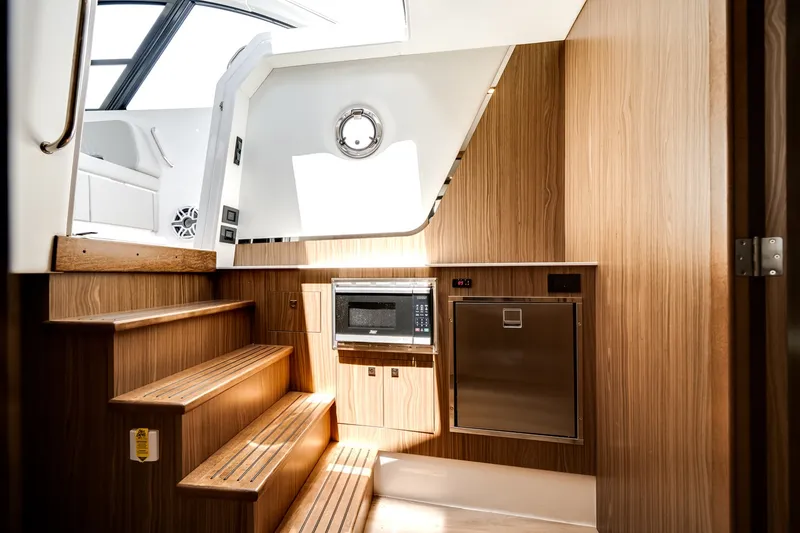 Slide: The Image of Interior of the 2026 Cruisers Yachts 50 GLS with wood paneling, stairs, microwave, and window. - 43