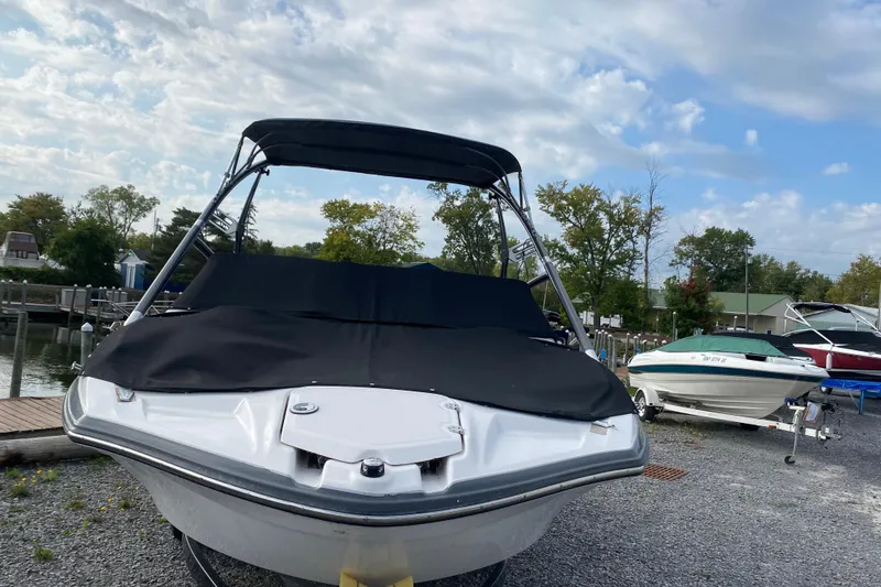 Slide: The Image of 2015 Yamaha Boats 212X with cover, parked on gravel near a dock. - 6