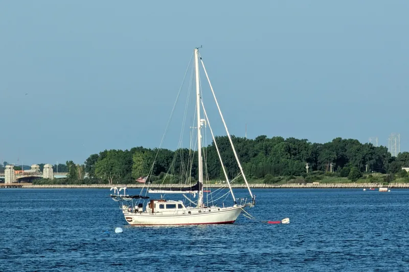 Slide: The Image of 1982 Shannon Pilothouse sailboat anchored on calm water with lush green shoreline. - 20