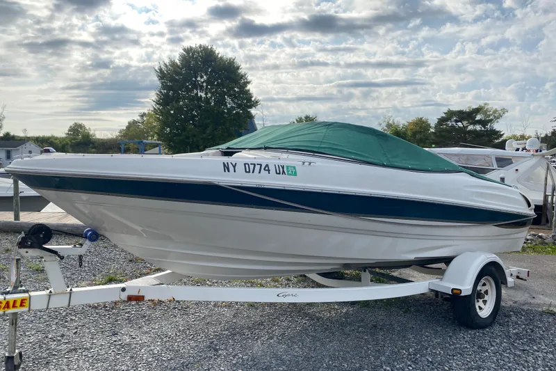 The Image of 1999 Ebbtide 2300 Bow Rider boat on trailer with green cover, parked outdoors. - 1