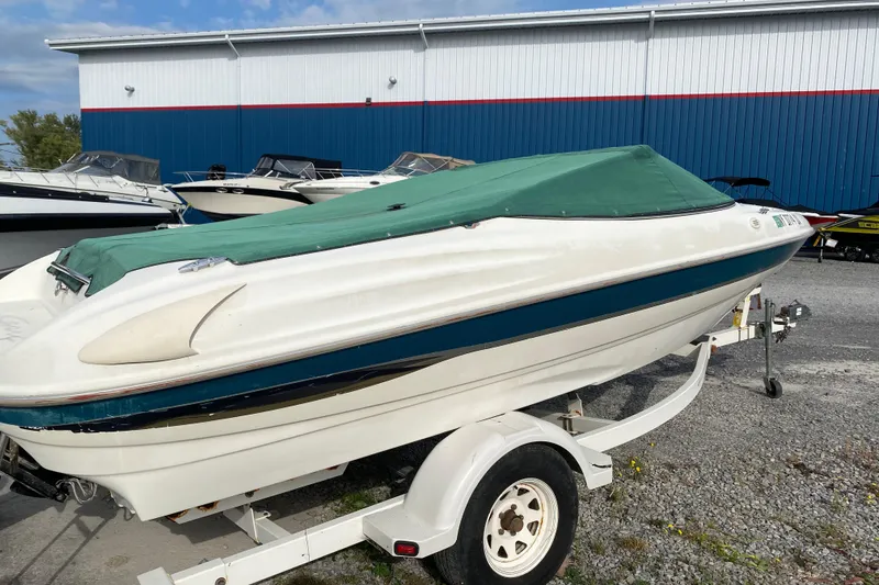 Slide: The Image of 1999 Ebbtide 2300 Bow Rider boat with green cover on trailer, parked outdoors. - 3