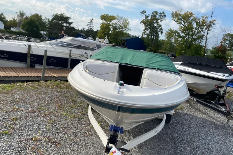 Slide: The Image of 1999 Ebbtide 2300 Bow Rider boat with green cover, parked on gravel near dock. - 5
