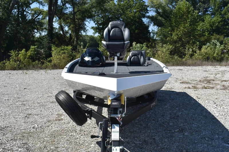 Slide: The Image of 2026 Lund 1875 Renegade boat on trailer, parked on gravel, surrounded by trees. - 2