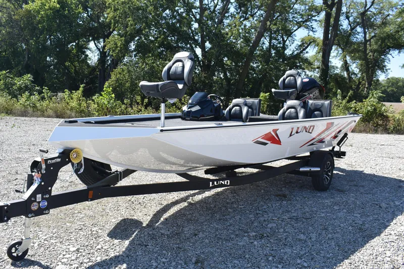 Slide: The Image of 2026 Lund 1875 Renegade boat on trailer, parked outdoors, surrounded by trees. - 3