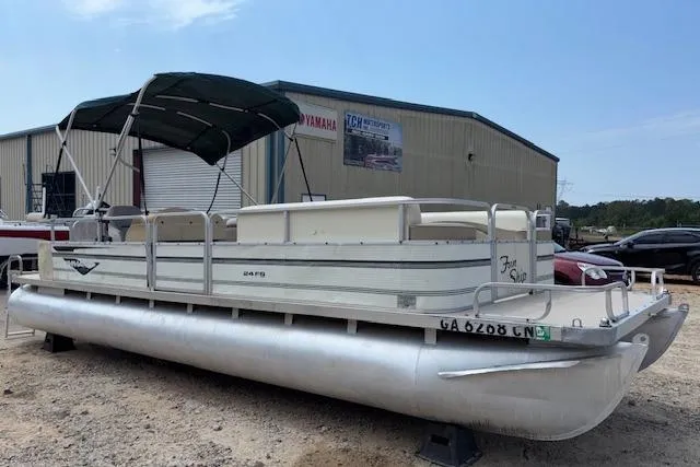 Slide: The Image of 1997 Grumman 24 FS pontoon boat with canopy, parked outdoors near a warehouse. - 1