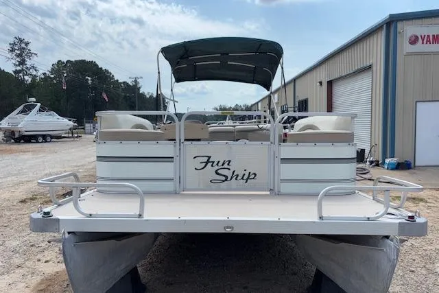 Slide: The Image of 1997 Grumman 24 FS pontoon boat with canopy, labeled "Fun Ship," parked near a warehouse. - 2