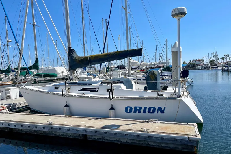 The Image of 1985 Hunter 31 sailboat named "Orion" docked in a marina under clear blue skies. - 0