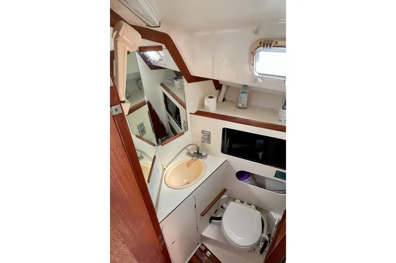 Slide: The Image of Compact bathroom in a 1985 Hunter 31 sailboat, featuring sink, toilet, and storage shelves. - 26