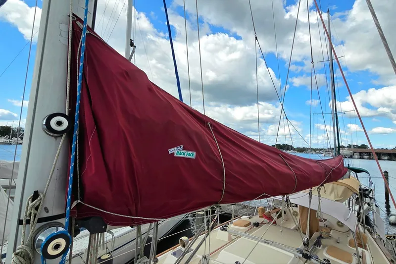 Slide: The Image of 1989 Island Packet 38 sailboat with maroon sail cover docked under a cloudy sky. - 16