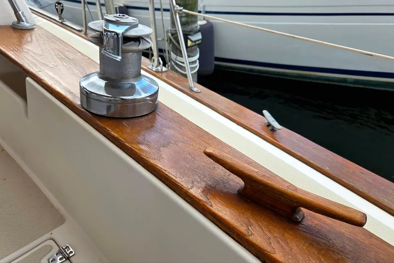 Slide: The Image of 1989 Island Packet 38 sailboat deck with winch and cleat, showcasing polished wood finish. - 18
