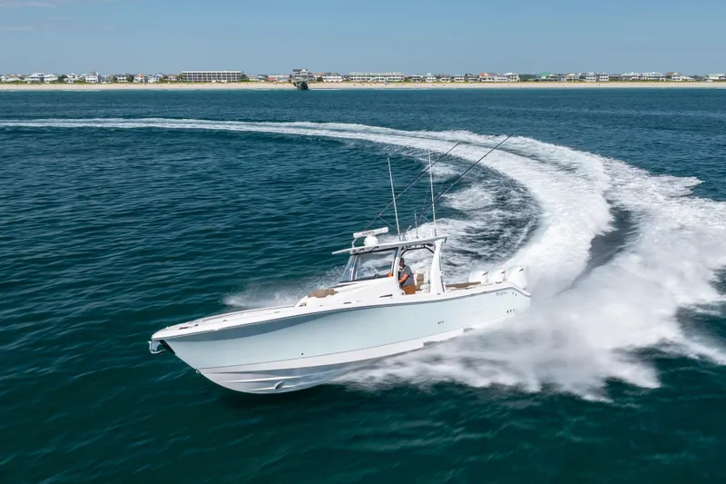 Slide: The Image of 2021 Edgewater 370CC boat cruising swiftly on open water near a coastal shoreline. - 27