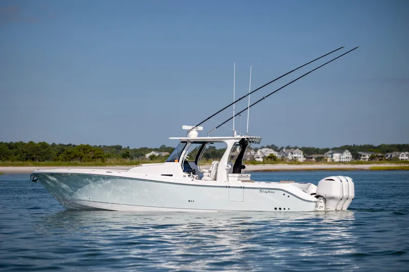 Slide: The Image of 2021 Edgewater 370CC boat on calm water with fishing rods, coastal background. - 3