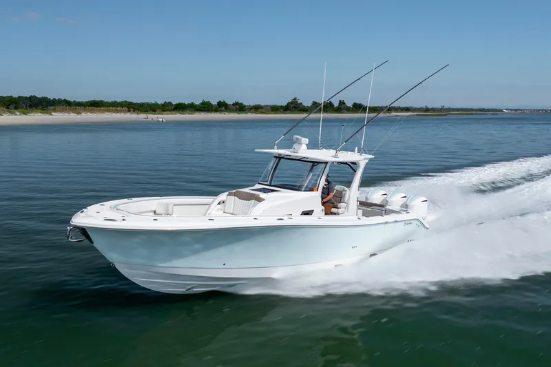 Slide: The Image of 2021 Edgewater 370CC boat cruising on calm waters near a sandy shoreline. - 32