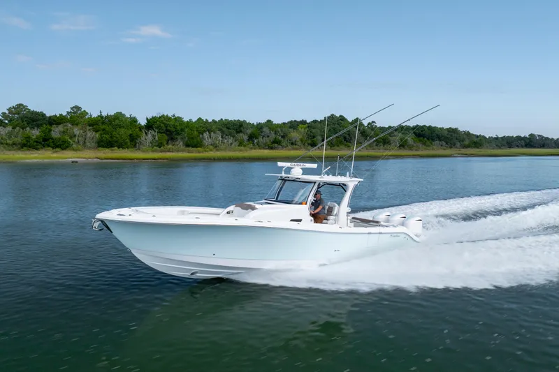 Slide: The Image of 2021 Edgewater 370CC boat cruising on a calm lake with lush green shoreline. - 36