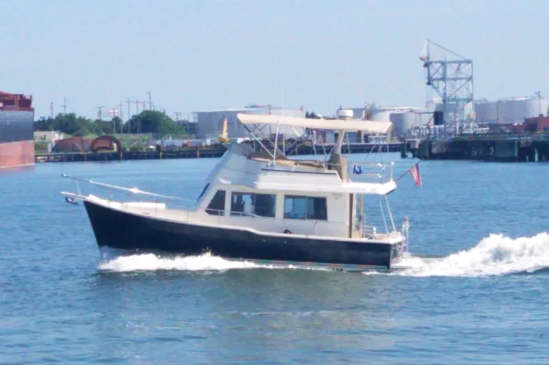Slide: The Image of 2008 Mainship 34 Trawler cruising on a sunny day near an industrial waterfront. - 38