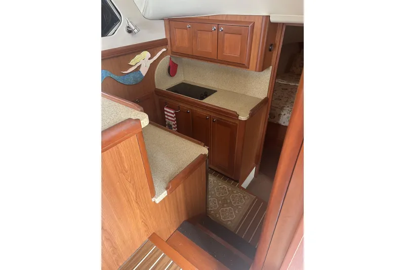 Slide: The Image of 2008 Mainship 34 Trawler interior with kitchenette, wooden cabinetry, and mermaid wall art. - 7