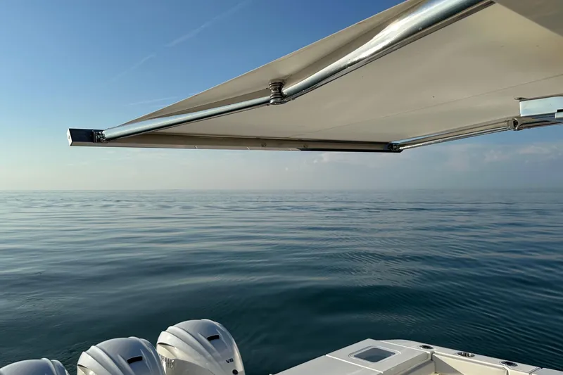 Slide: The Image of 2024 Pursuit OS 445 Offshore boat with awning, calm sea, and clear sky. - 41