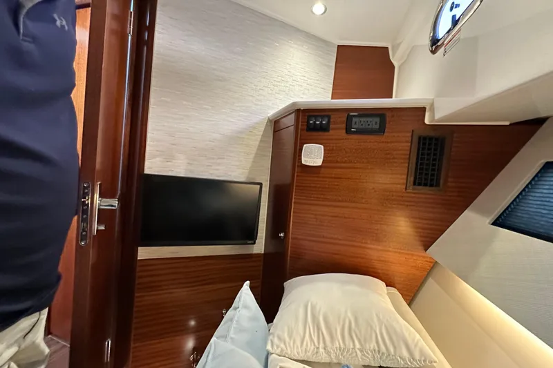 Slide: The Image of 2024 Pursuit OS 445 Offshore cabin interior with bed, TV, and wood paneling. - 65
