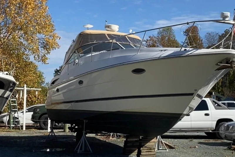 Slide: The Image of 2003 Cruisers Yachts 3470 Express on dry dock, surrounded by autumn trees and vehicles. - 3