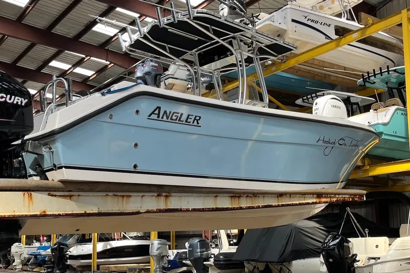 Slide: The Image of 2011 Angler 2600 CC boat in storage, featuring a light blue hull and dual outboard motors. - 11
