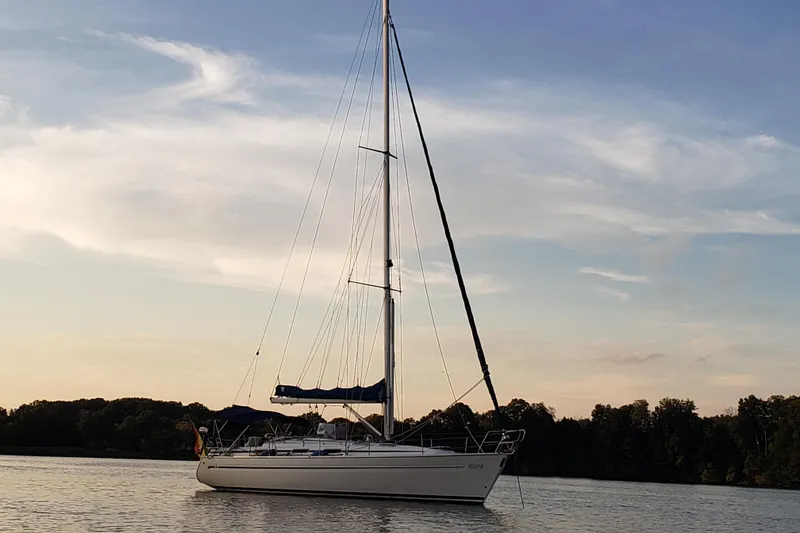 The Image of Sailboat Bavaria 40 (2002) on calm water at sunset with trees in the background. - 0