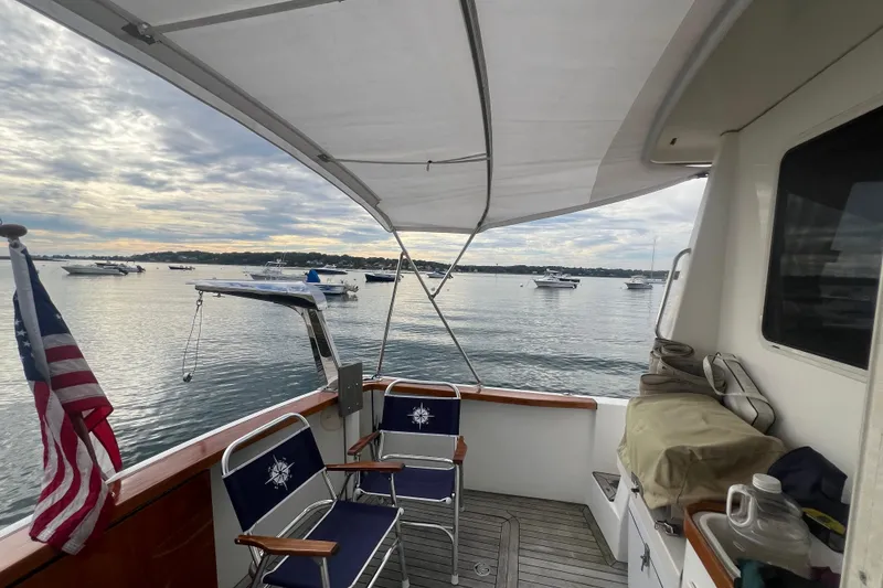 Slide: The Image of 2004 Sabre 36 Hardtop Sedan boat deck with chairs, American flag, and scenic harbor view. - 16