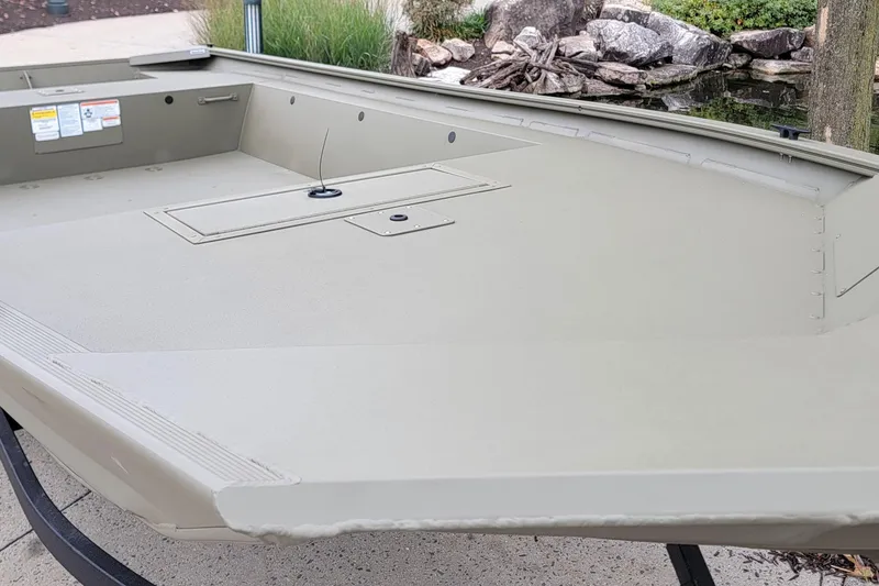 Slide: The Image of 2026 Tracker Grizzly 1754 Utility boat, beige interior, near a pond with rocks. - 2