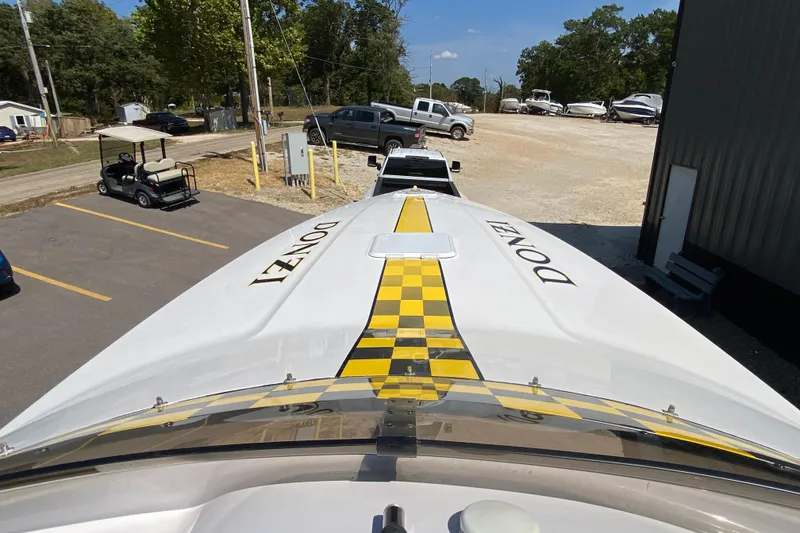 Slide: The Image of 2001 Donzi ZX boat with yellow checkered stripe, parked near vehicles and trees. - 3