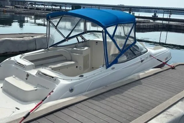 Slide: The Image of 2005 Stingray 220 DR boat docked with blue canopy, calm water background. - 2