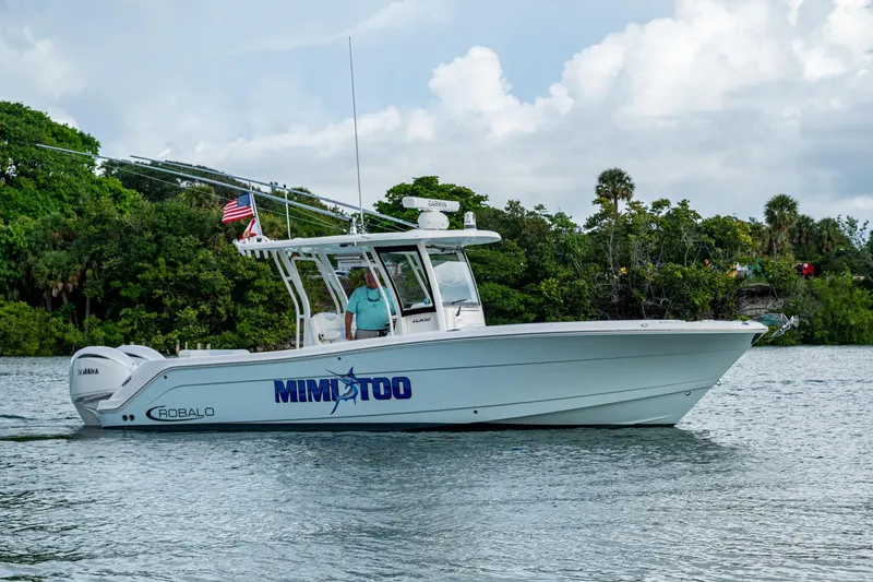 Slide: The Image of 2023 Robalo R302 Center Console boat on water, lush greenery in background. - 1