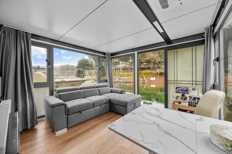 Slide: The Image of Modern houseboat interior with gray sofa, marble table, and large windows overlooking water. Gospel 39, 2024. - 7