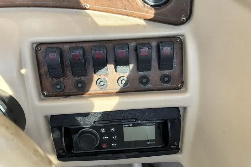 Slide: The Image of Control panel of a 1999 Ebbtide 2300 boat with switches and a Fusion stereo. - 25
