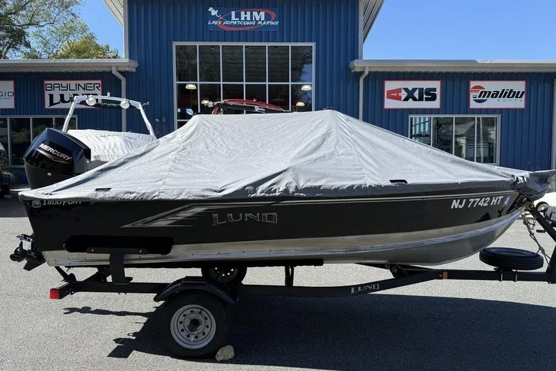Slide: The Image of 2023 Lund 1400 Fury SS boat with cover on trailer, parked outside marine store. - 3